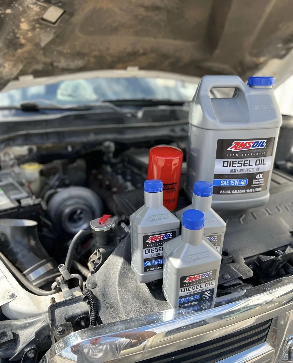 Synthetic 15W-40 diesel oil and a new oil filter set out for a diesel oil change, turbocharger visible under the open hood