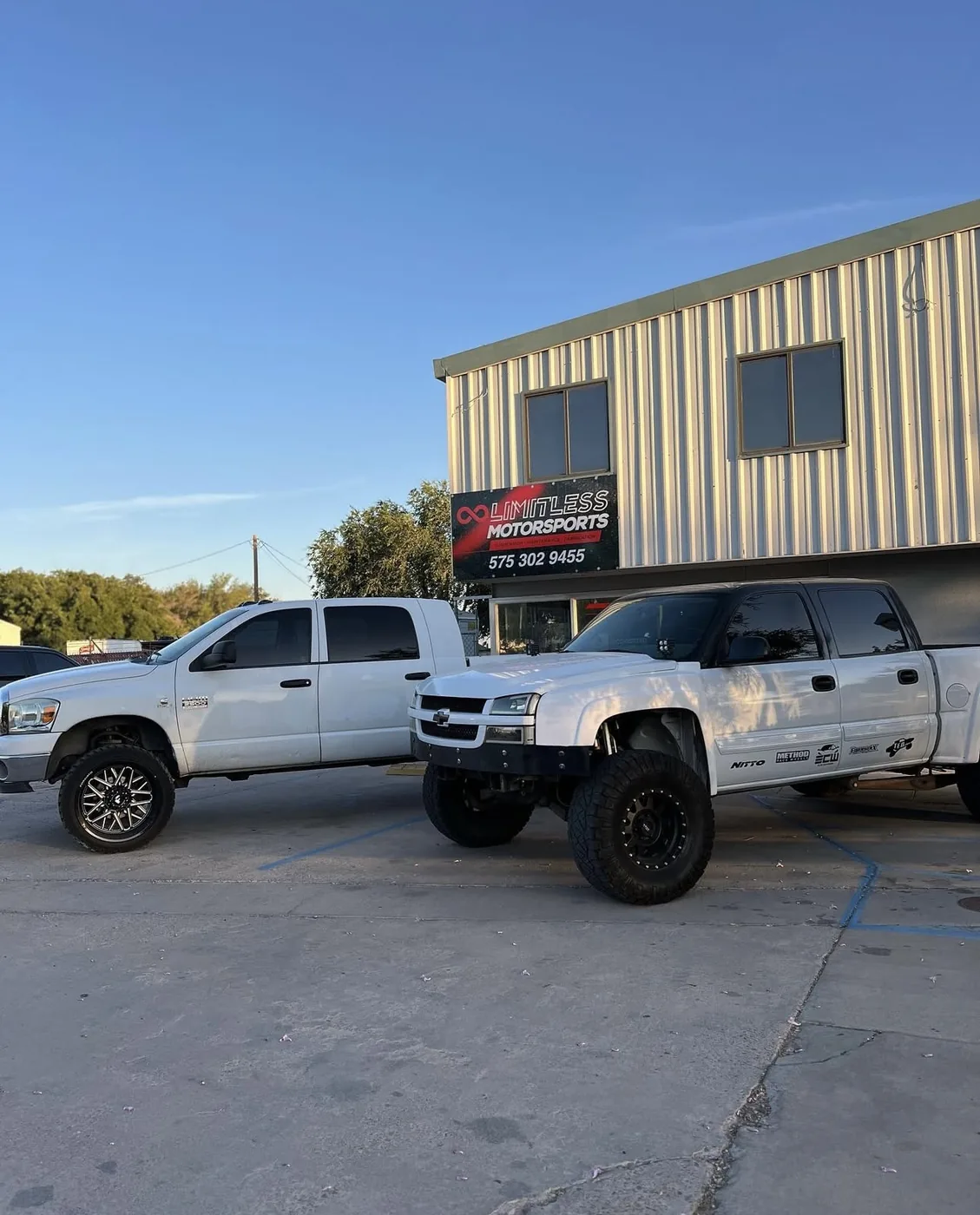 A white Ram 2500 diesel and a lifted Chevrolet Silverado 2500HD with a custom front bumper parked outside the Limitless Motorsports shop on West Picacho