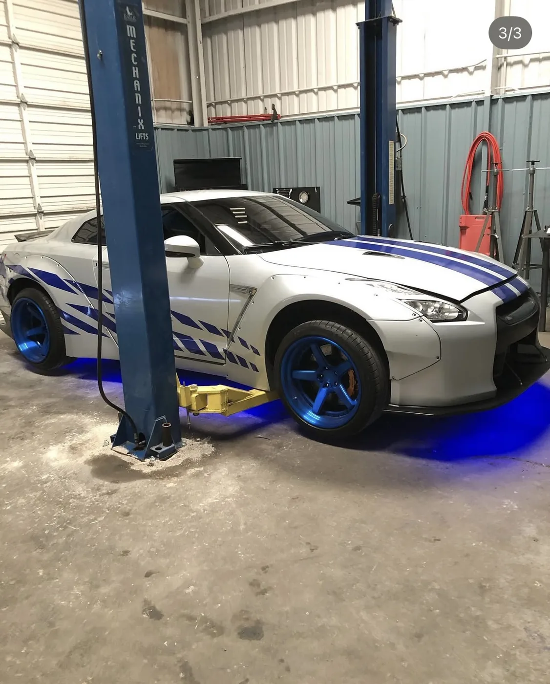 Silver Nissan GT-R with blue graphics and blue wheels raised on a two-post lift at Limitless Motorsports